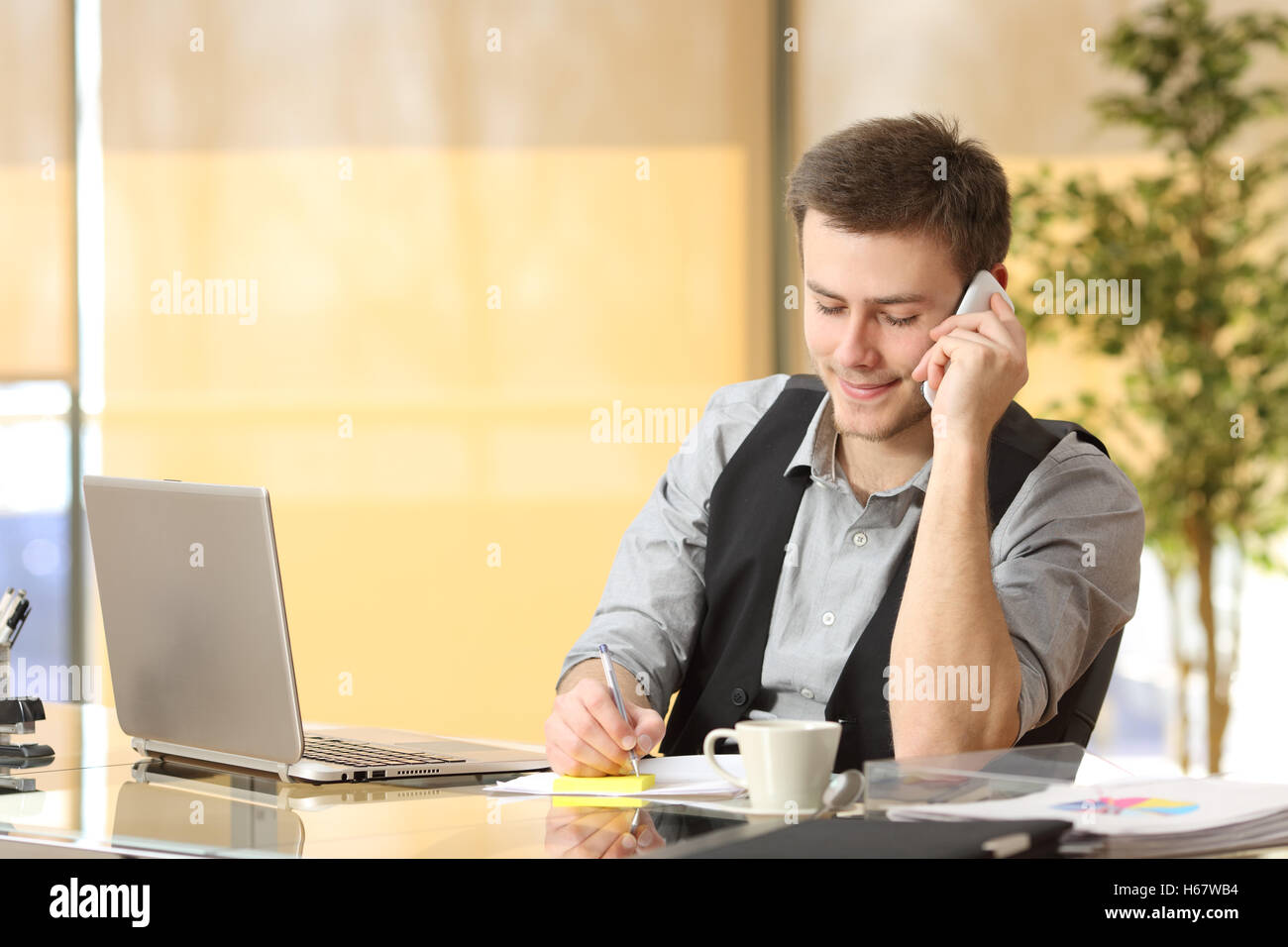 Entrepreneur working on the phone and writing notes sitting in a desk at office Stock Photo