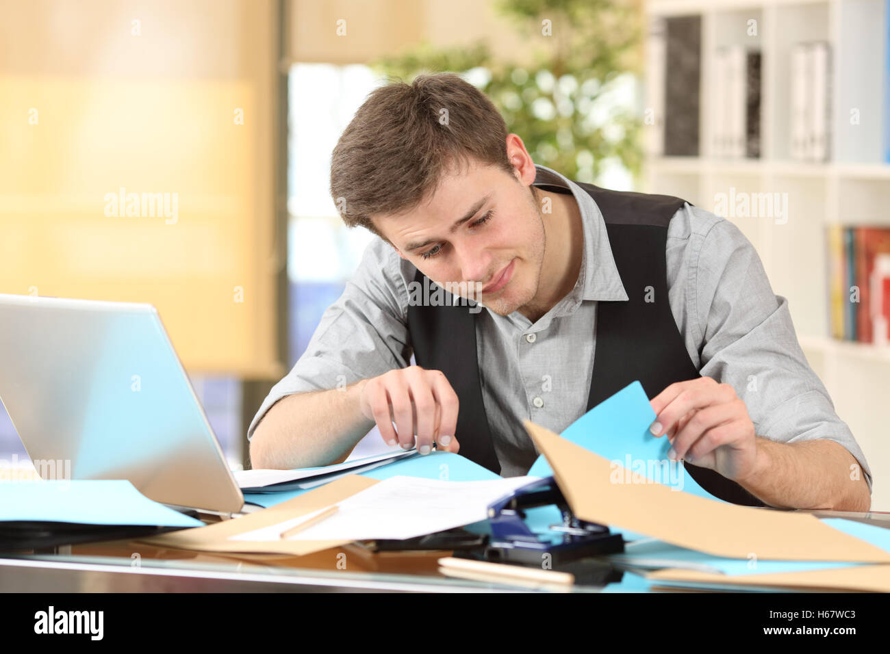 Incompetent messy businessman with disorganized desk searching lost documents at office Stock Photo