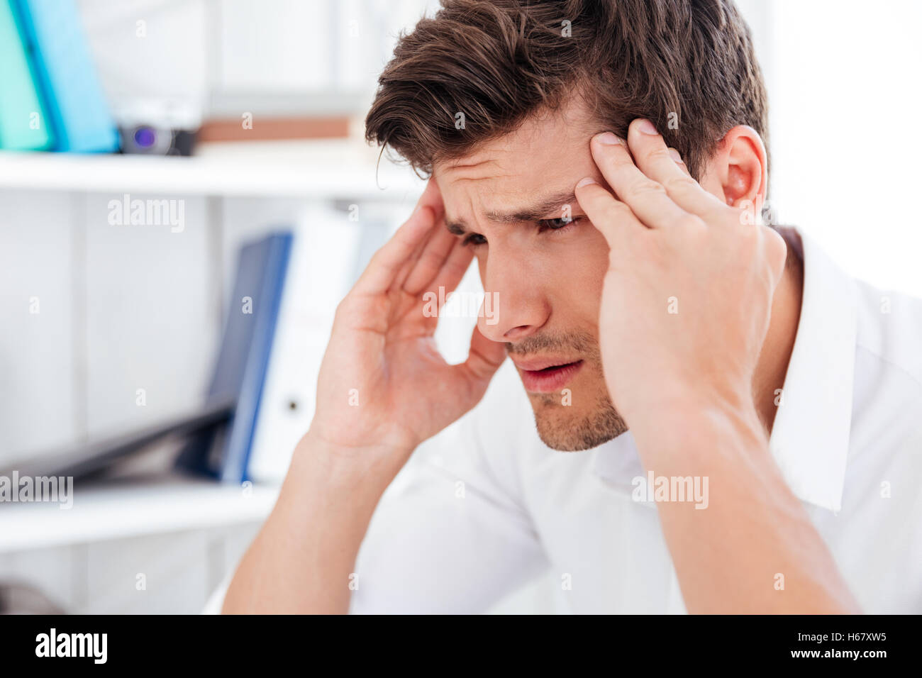 Close up portrait of a tired young businessman touching his temples and having a headache in office Stock Photo