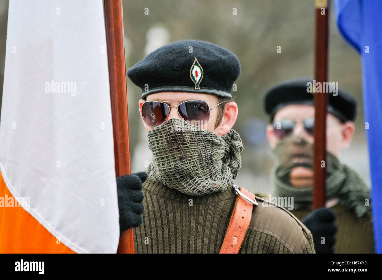 Men dressed in Irish paramilitary uniforms, with their faces covered by military scrim scarves carry Irish flags in Milltown cemetery, during the annu Stock Photo