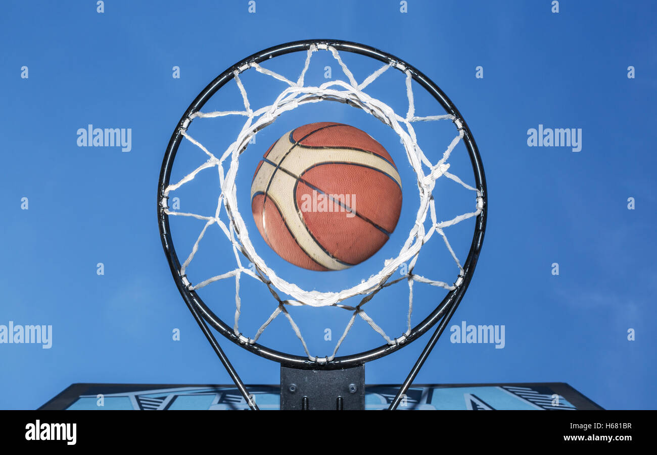 Basketball falling through the net. Blue sky on the background. Stock Photo