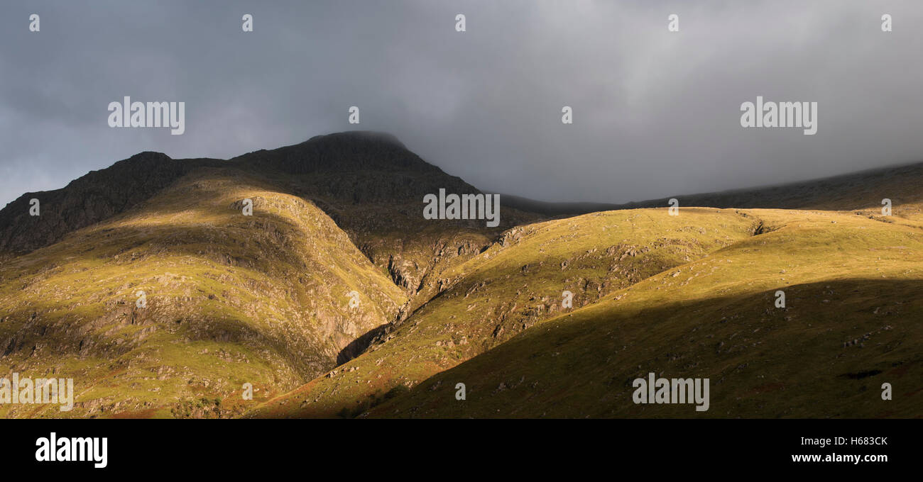 Rain cloud forming thick fog descending from steep mountainside bading ...