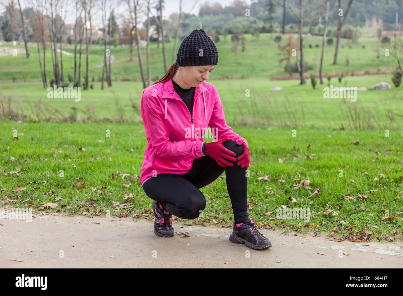 Young female athlete hurting from a knee injury on a cold winter day on the track of an urban park. Stock Photo