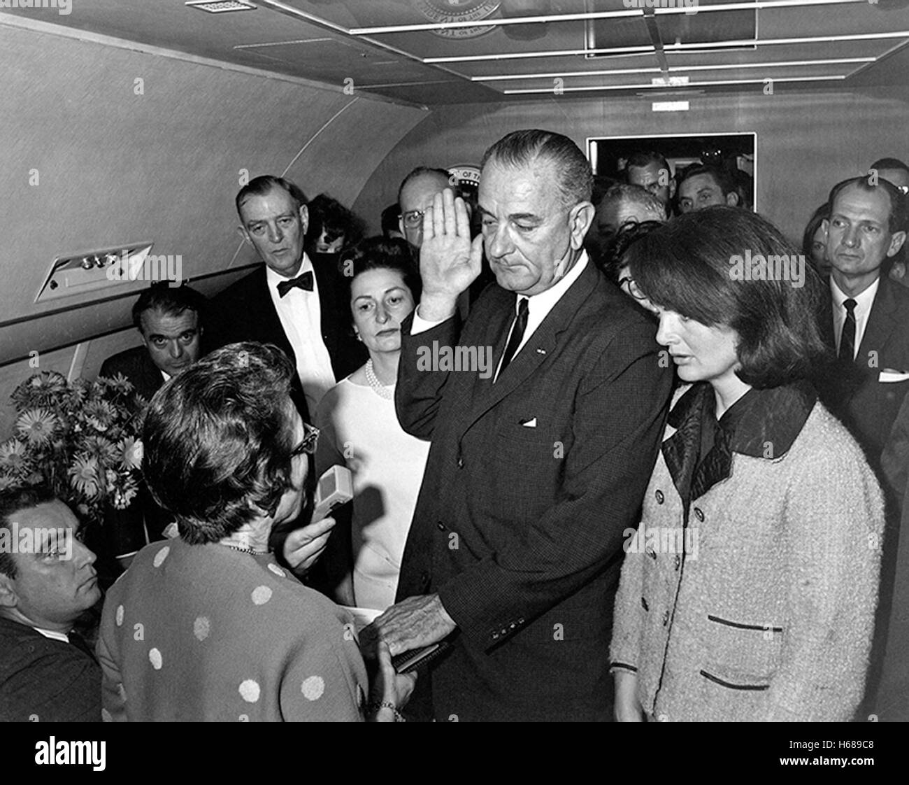 Judge Sarah T. Hughes administers the Presidential Oath of Office to Lyndon Baines Johnson aboard Air Force One on November 22, 1963, at Love Field, Dallas Texas. Mrs. Johnson, Mrs. Kennedy, Jack Valenti, Cong. Albert Thomas, Cong. Jack Brooks, Associate Press Secretary Malcolm Kilduff (holding microphone) and others witness. Photograph by Cecil Stoughton/The White House Stock Photo