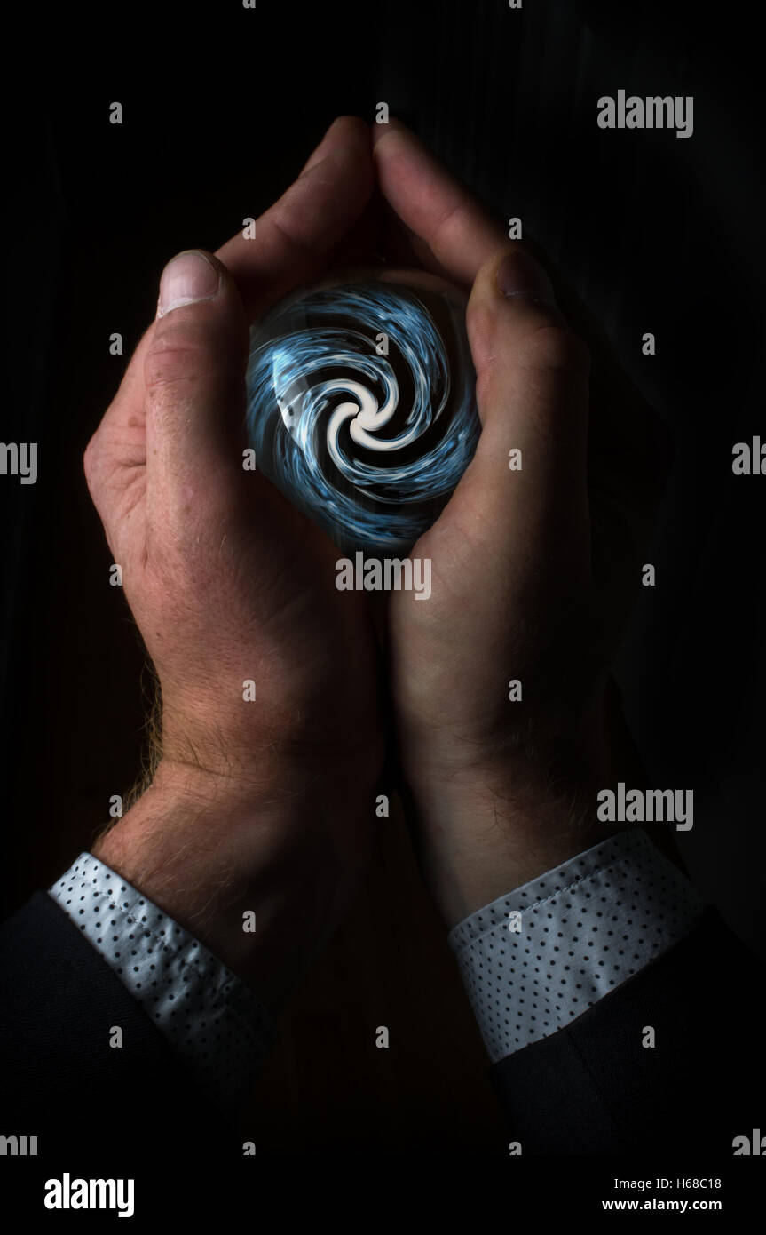 Hands holding magic crystal ball with smoky hypnosis spiral Stock Photo