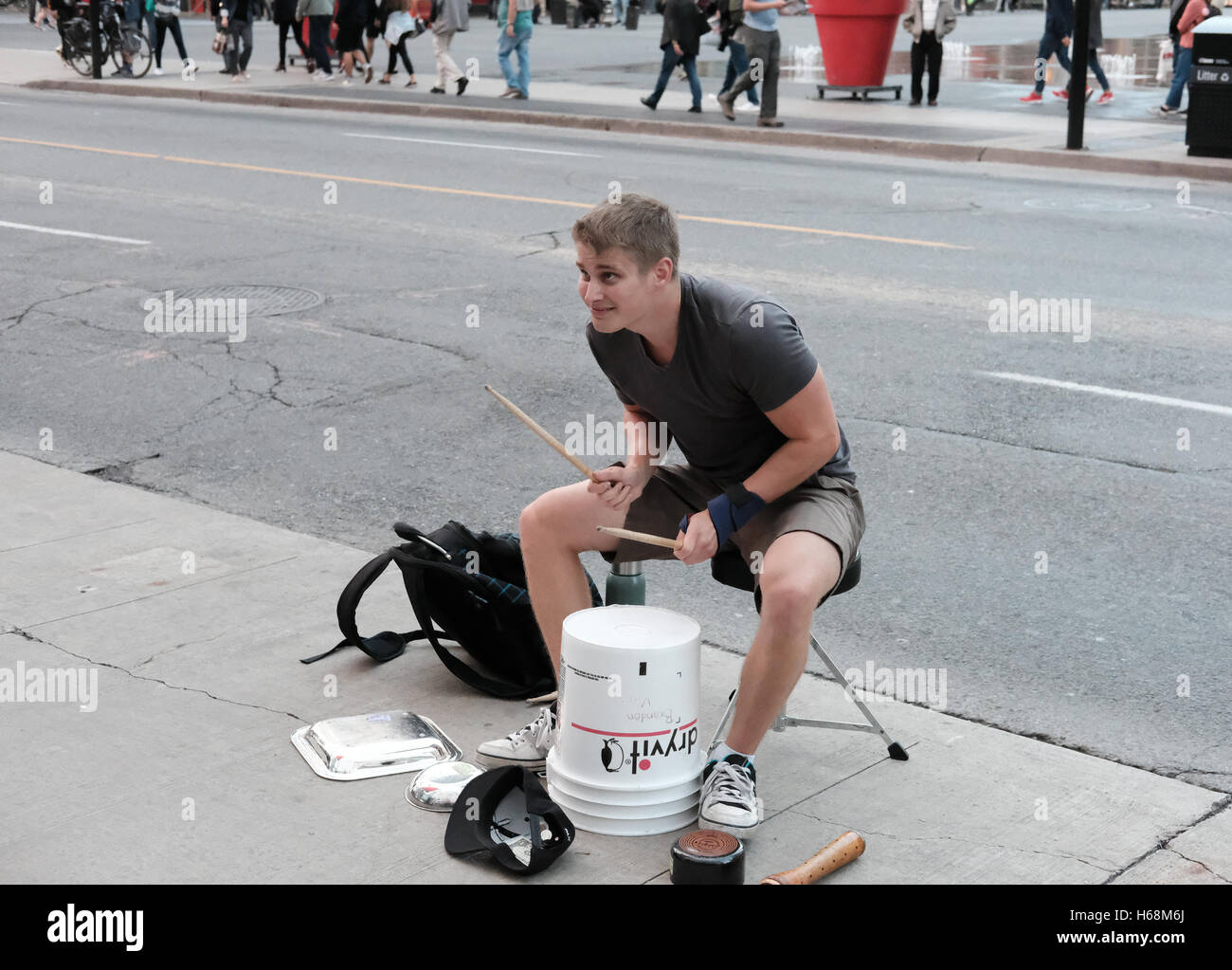 Young adult seen playing improvised drums in a busy city center at rush