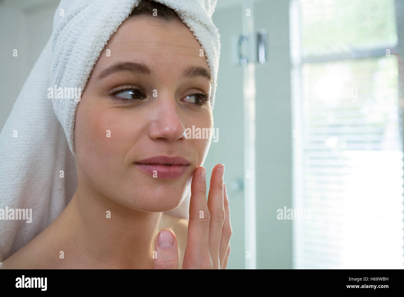 Woman applying moisturizer cream on her face in bathroom Stock Photo