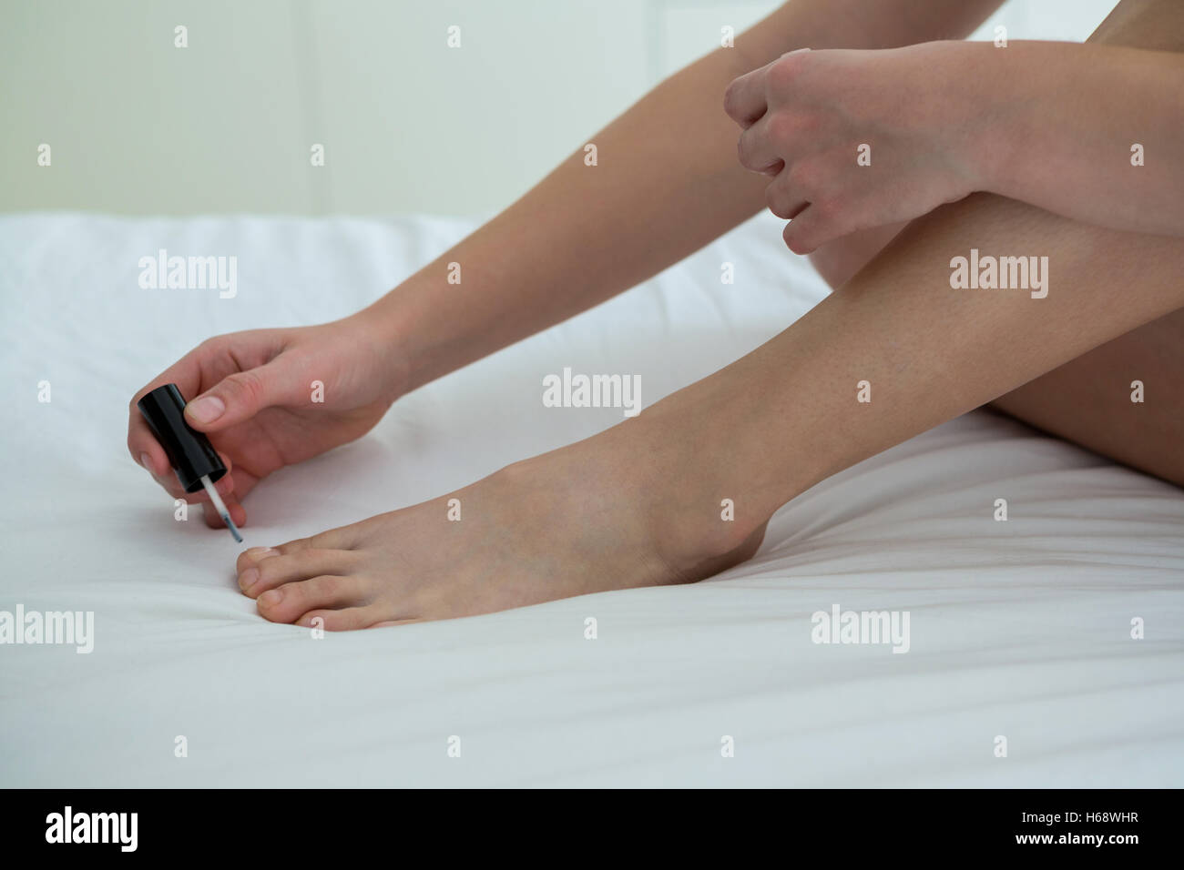 Woman applying nail polish on her toe nails in bedroom Stock Photo