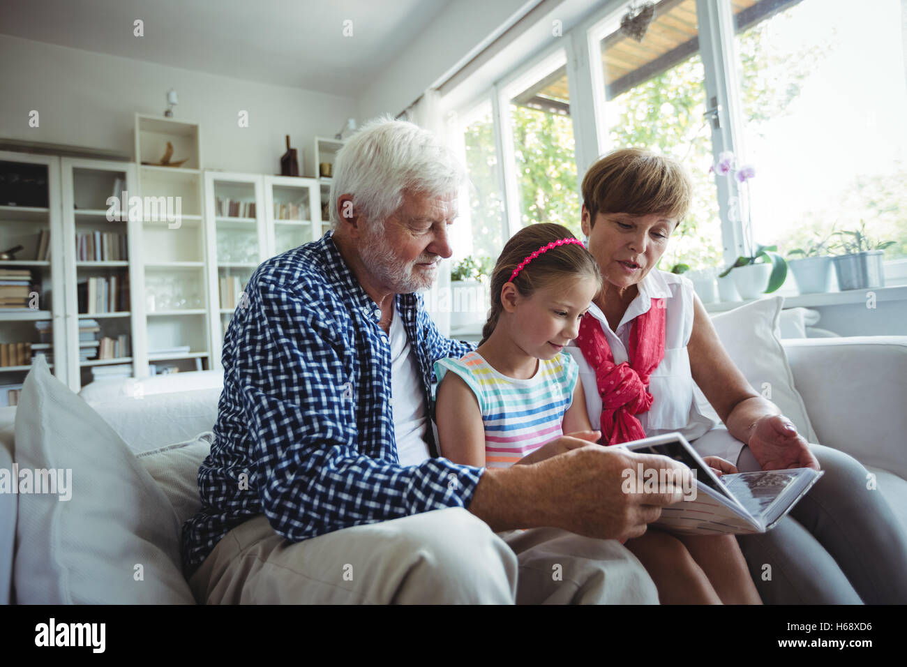 Grandparents and granddaughter looking at photo album in living room Stock Photo