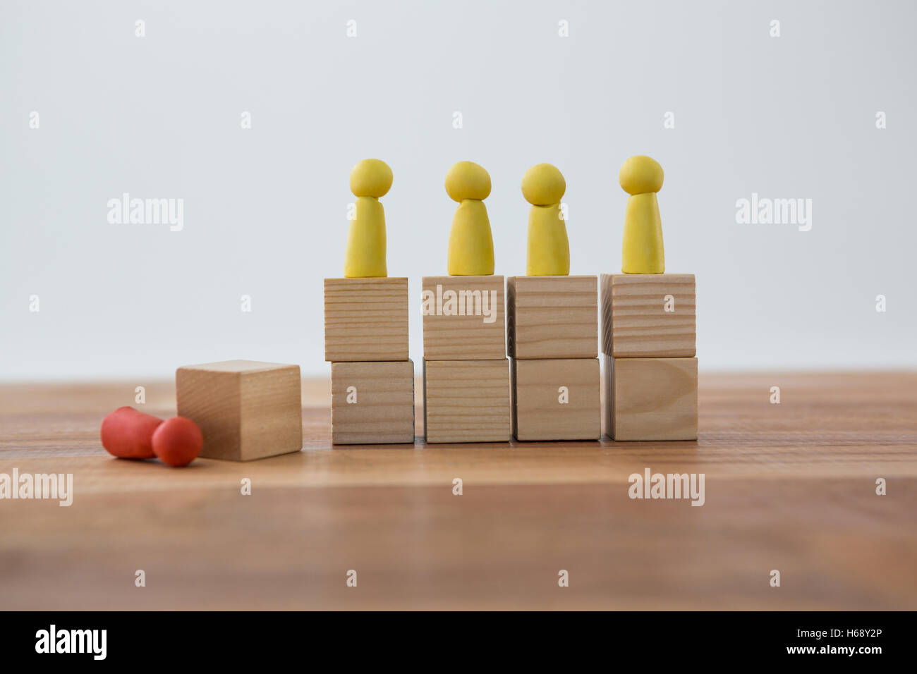 Yellow Figurines on wooden blocks in a row and red figurine fallen on ground Stock Photo