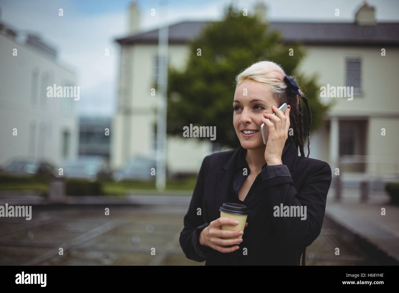 Businesswoman talking on mobile phone while holding disposable coffee cup Stock Photo