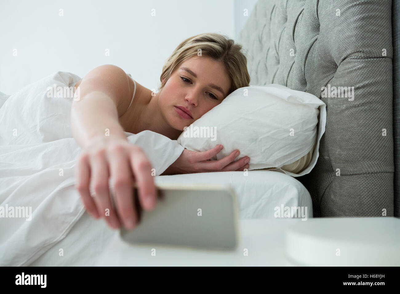 Young woman waking up with mobile alarm clock Stock Photo