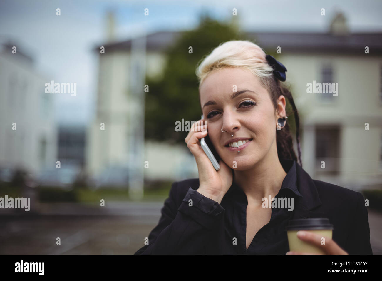 Portrait of businesswoman talking on mobile phone while holding disposable coffee cup Stock Photo