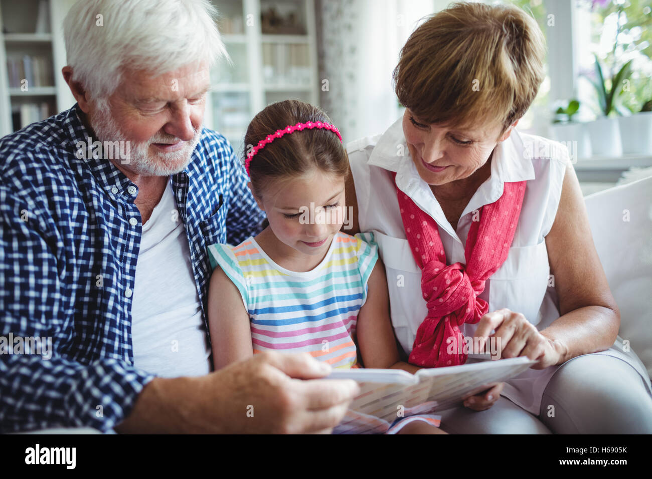 Grandparents and grand daughter looking at photo album in living room Stock Photo