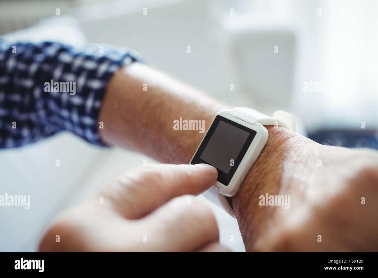 Senior man adjusting a time on smartwatch in living room Stock Photo