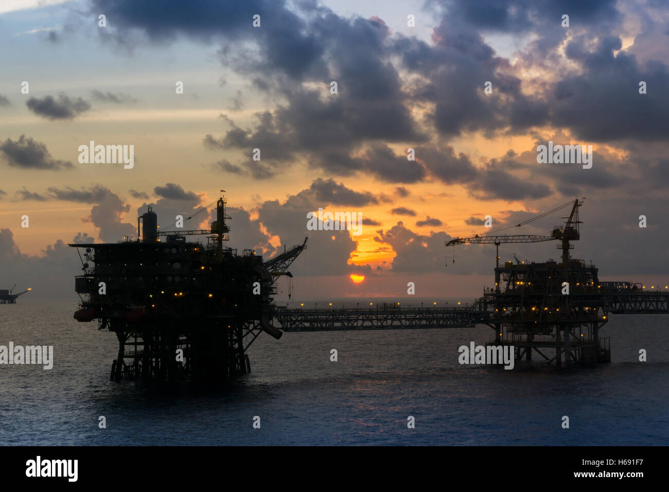 Silhouette of oil rigs connected with bridge in the evening at oilfield Stock Photo