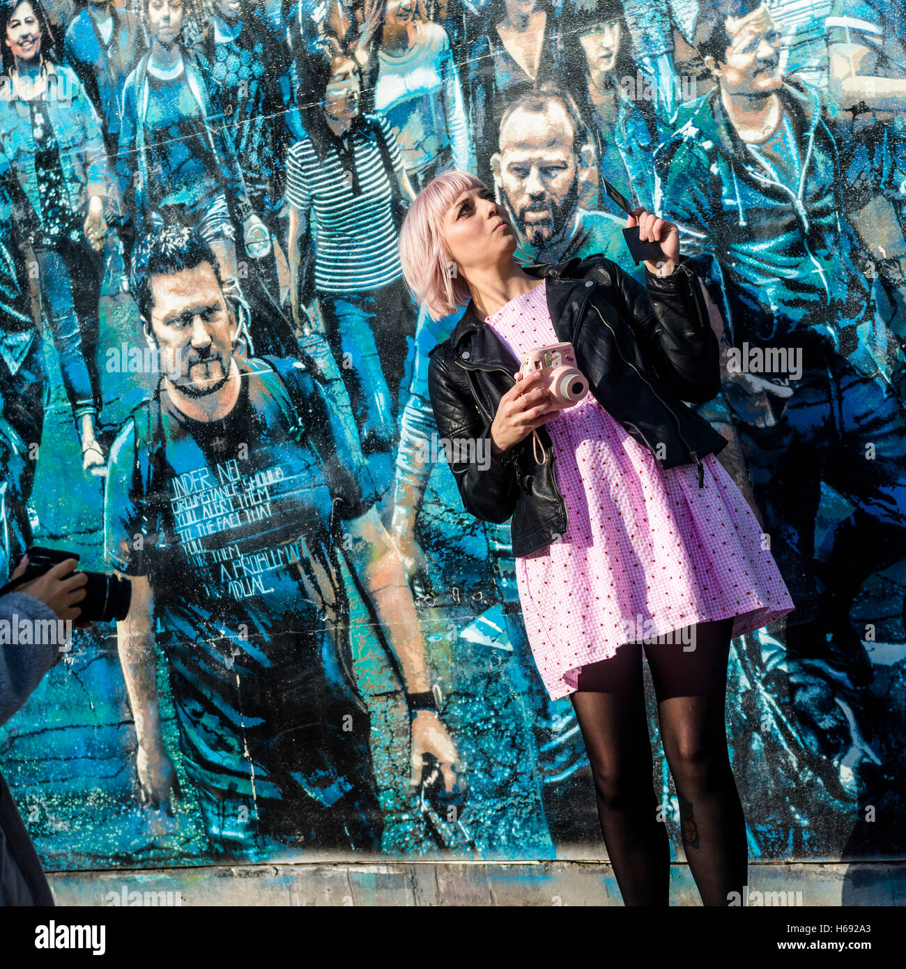 New York, NY 23 October 2016 - Woman in Pink taking a selfie in front of  Logan Hicks' mural entitled Story Of My Life . The mural features a crowd of people he photographed on the corner of Spring and Greene Street. Stacy Walsh Rosenstock Stock Photo