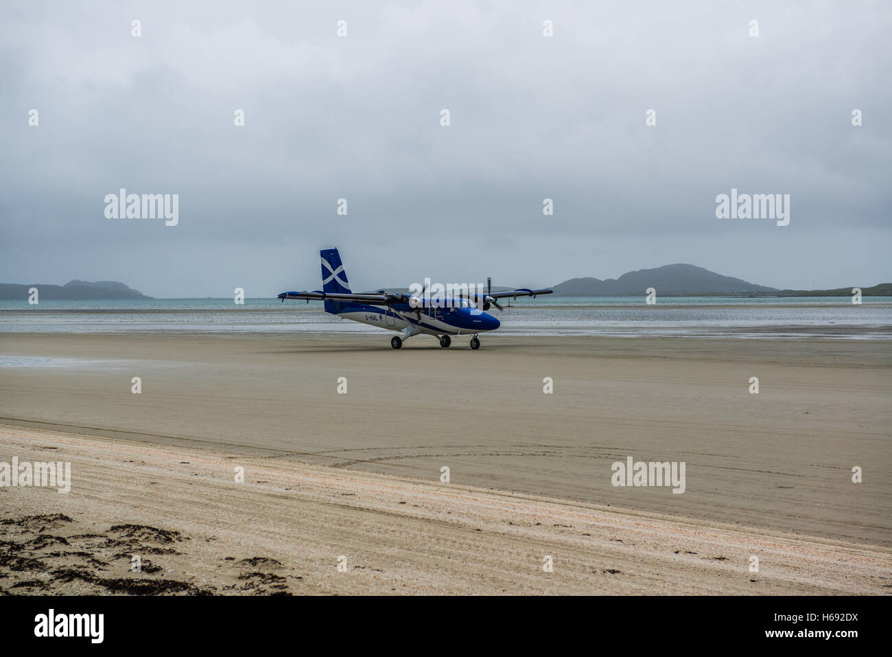 A Loganair flight from Glasgow lands on  An Tràigh Mhòr beach (English: The Big Beach) which is used as a runway. Planes can only land and take off at low tide meaning that the timetable varies. Voted the world's most stunning landing spot, Barra's airport is the only airport in the world to have scheduled flights landing on a beach. The aircraft currently in operation on Barra is the de Havilland Canada DHC-6 Twin Otter, flown by Loganair on services to Glasgow. Stock Photo