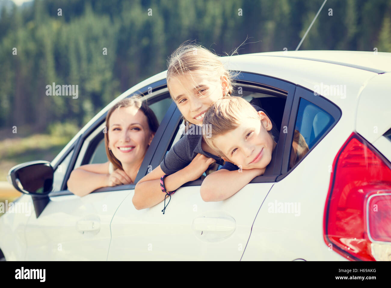 Happy young woman and her children sitting in a car and look out from windows. Family travel warm color toned image Stock Photo