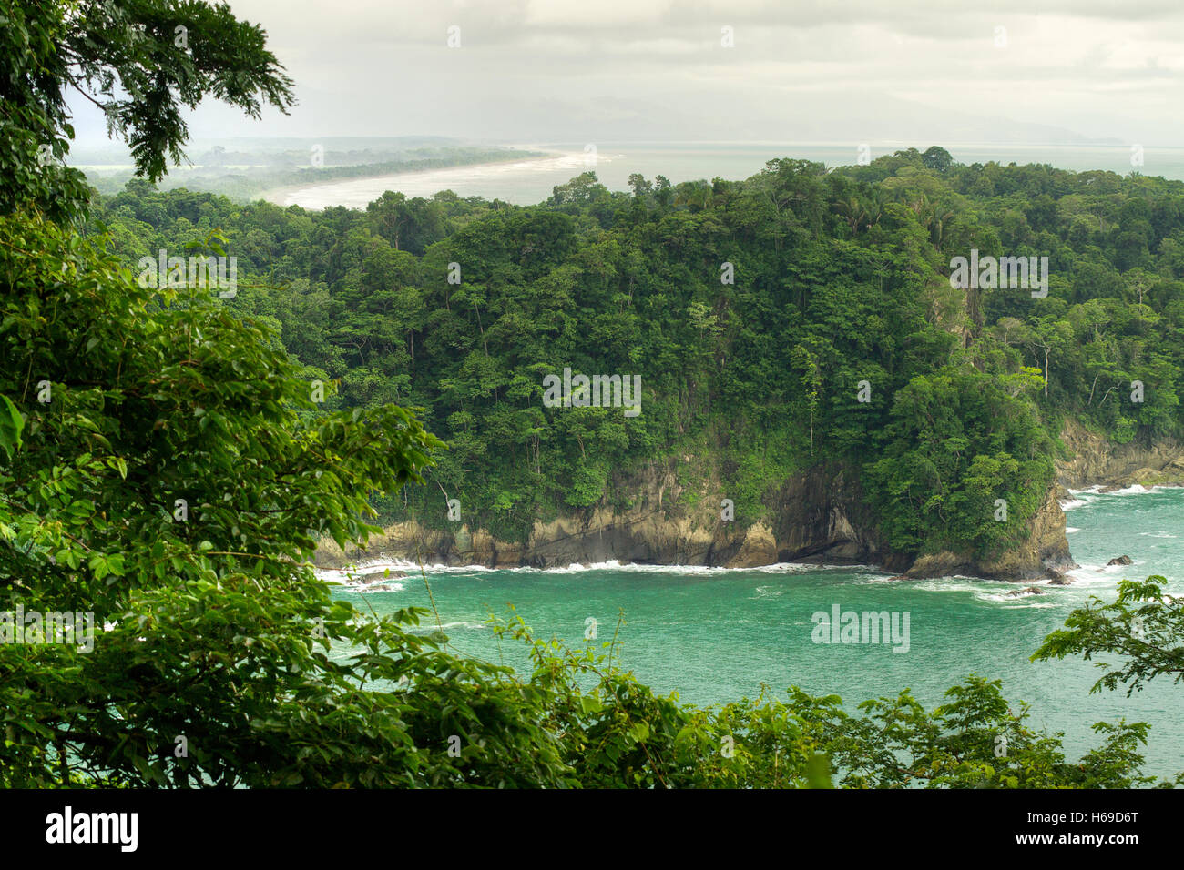 View from a hill in the middle of the jungle to a green and lush coastline in the tropics and blue-green ocean with a background Stock Photo