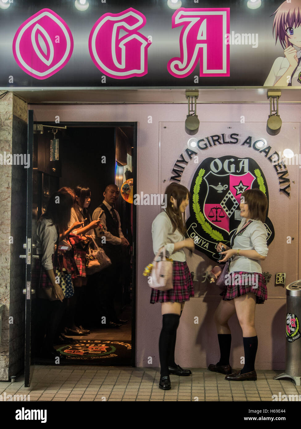 Young women in school girl uniform chat as they wait for clients  outside hostess club with schoolgirl theme, red light district, Omiya, Saitama Japan Stock Photo