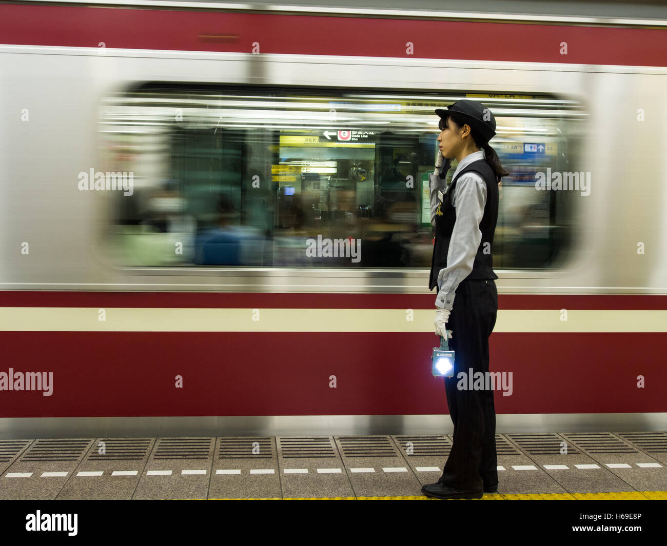 Woman railway worker with signaling lamp on platform as Japanese commuter train leaves station Stock Photo