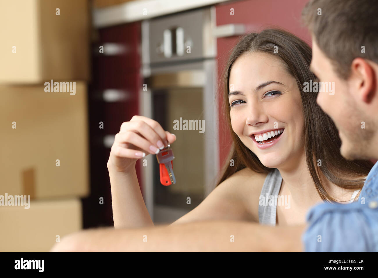 Happy new flat couple of owners showing keys sitting in the floor of the kitchen while moving home Stock Photo
