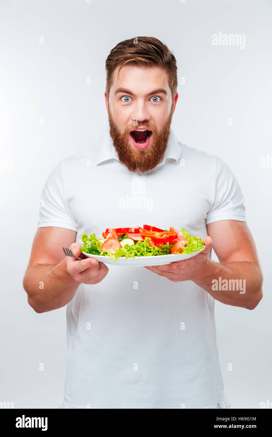 Young smiling man holding fork to eat fresh vegetable salad meal