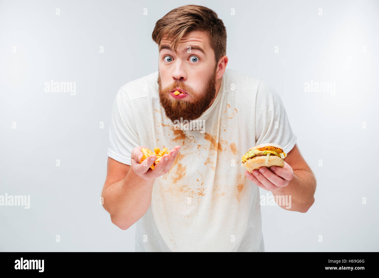 Excited hungry bearded man greedily eating hamburgers isolated on white background Stock Photo