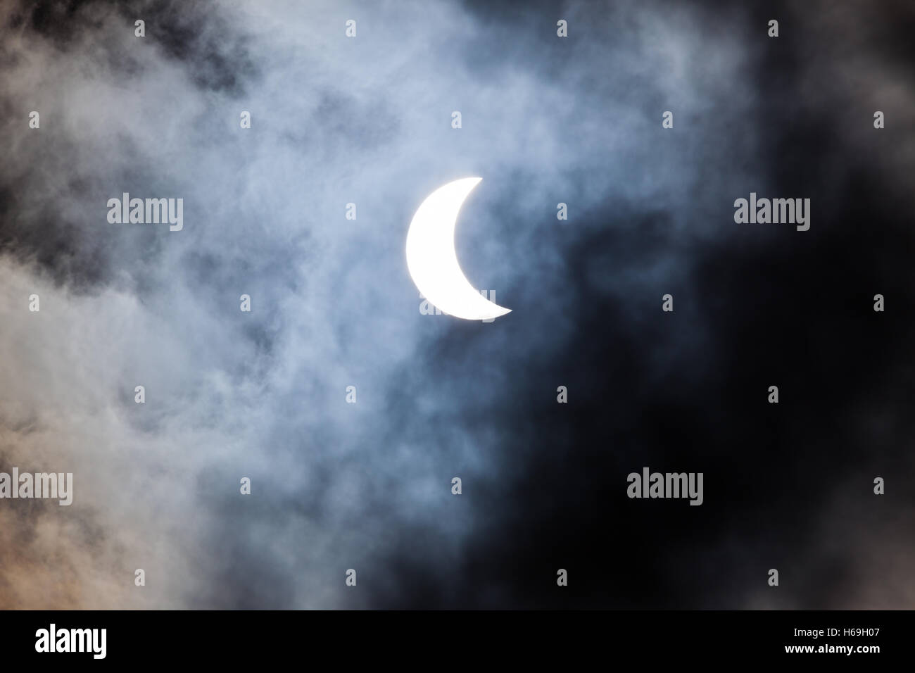 Partial solar eclipse through clouds Stock Photo