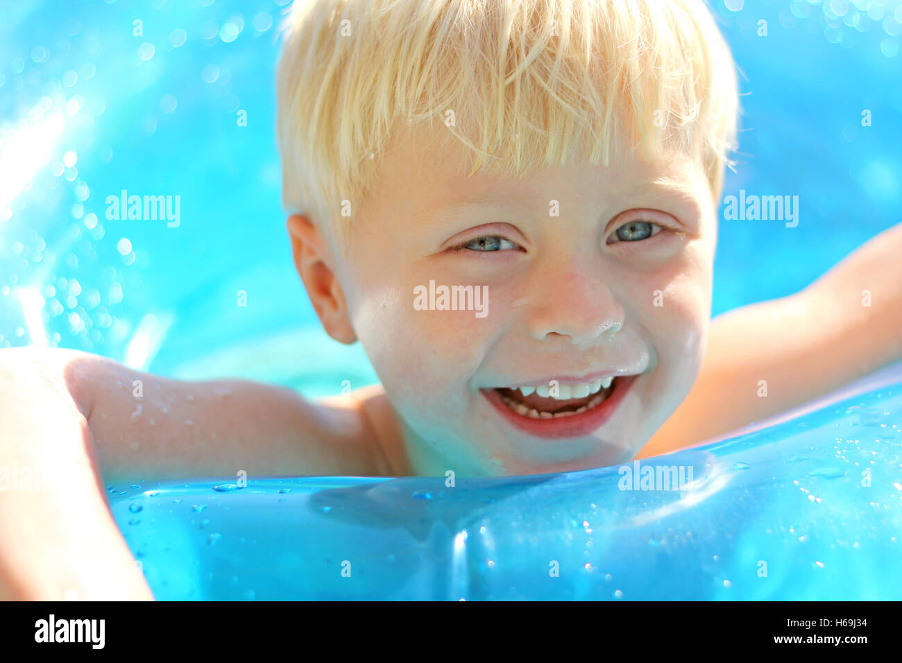 A cute, blonde, three year old boy child is laughing as he floats on a