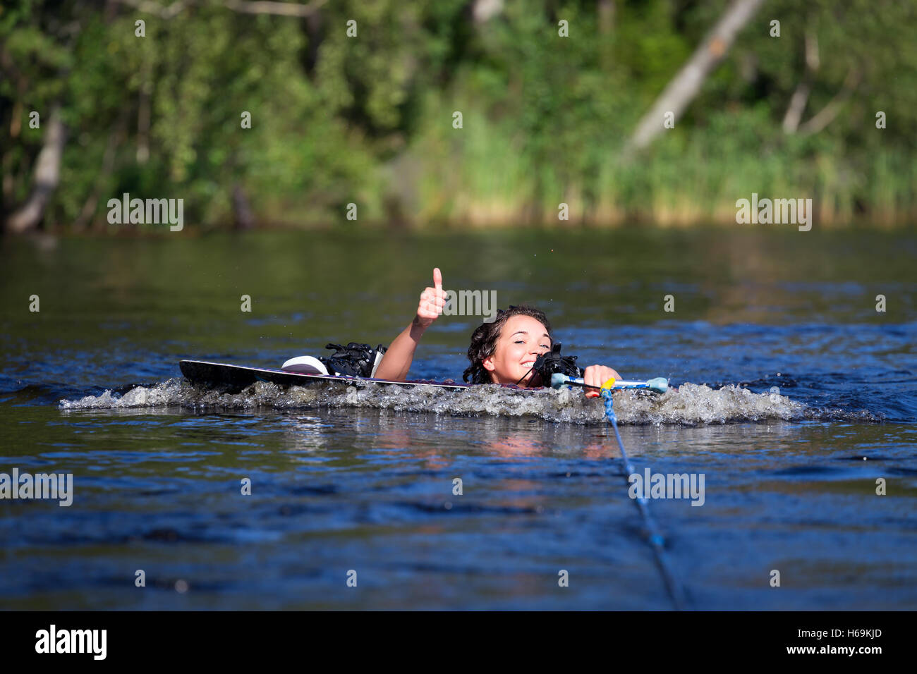 Young pretty slim brunette woman riding wakeboard on wave of motorboat in a summer lake Stock Photo
