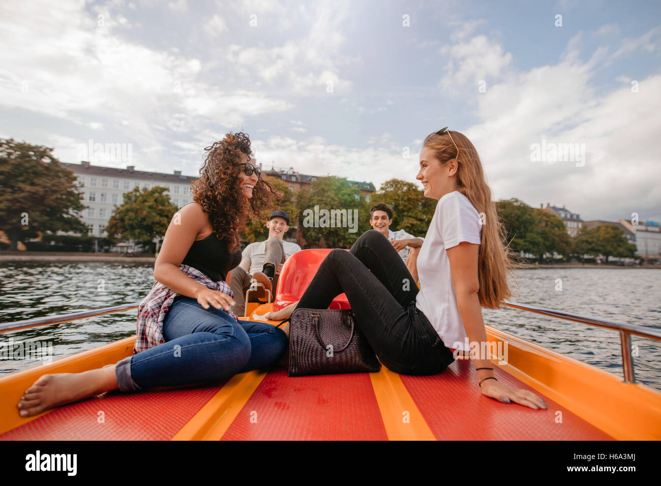 Shot of teenage girls sitting in the front of a boat in lake with male friends pedaling in background. Teenage friends relaxing Stock Photo