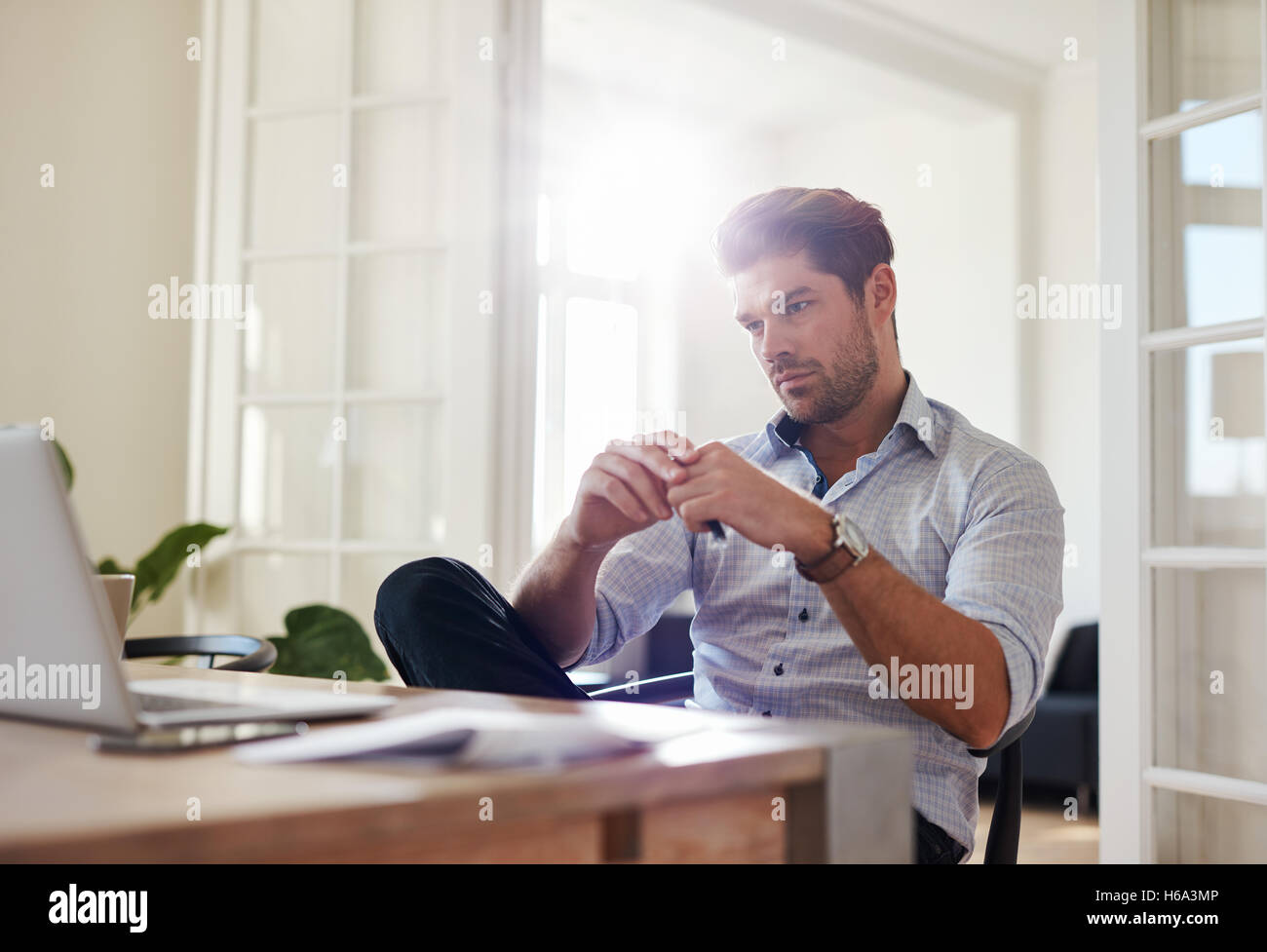 Shot of young man sitting at table looking at laptop and thinking. Thoughtful businessman working at home office. Stock Photo