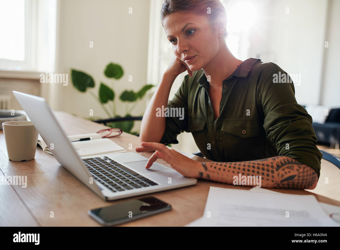 Shot of beautiful young woman working from home using laptop. Female sitting at table and surfing internet on laptop computer. Stock Photo