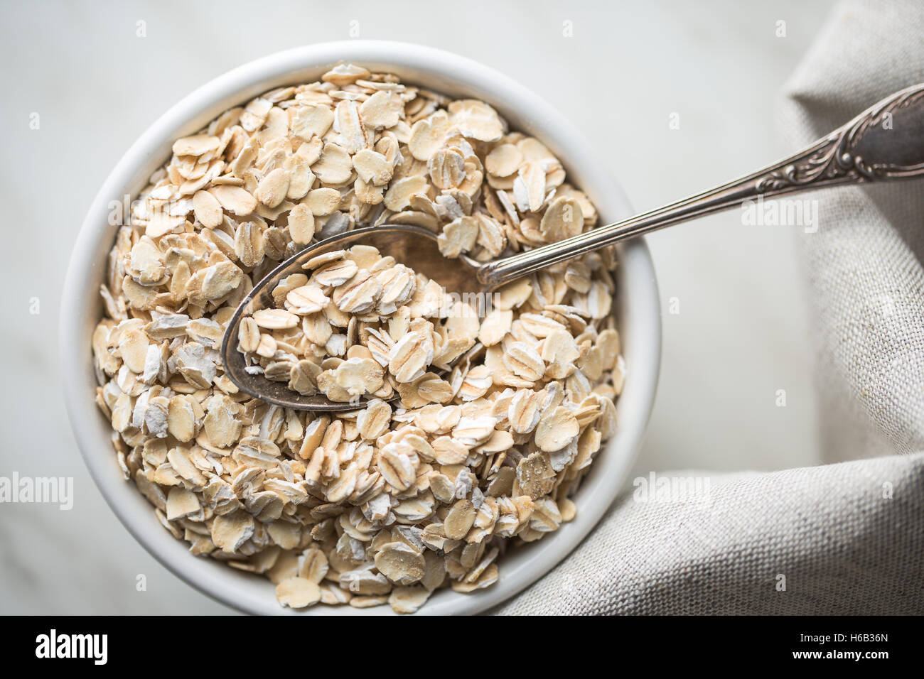 Dry rolled oatmeal in bowl with spoon. Top view. Stock Photo