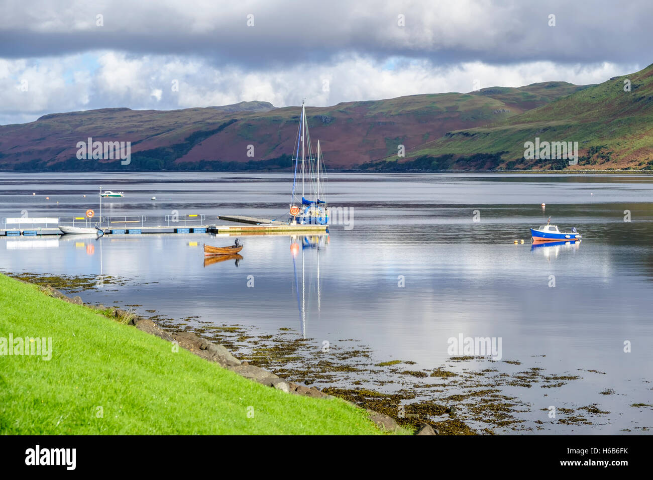 Boats and their reflections on the beautiful calm waters of Loch Harport at Carbost Isle of Skye Scotland with hills of purple h Stock Photo