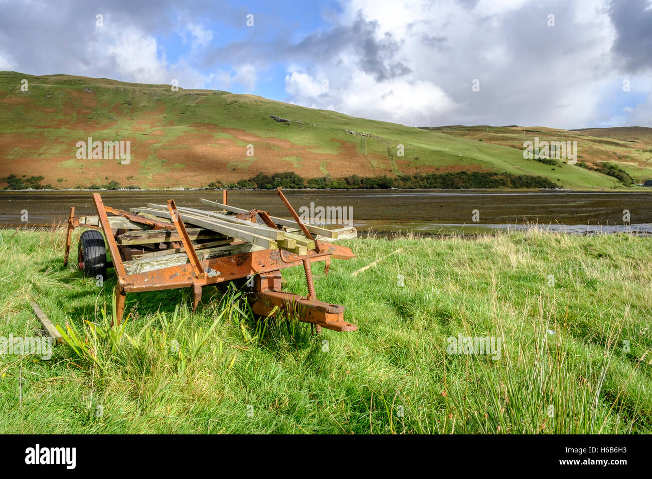 Old rusting farm trailer full of planks of timber on grass by the shore of Loch Harport Isle of Skye Scotland Stock Photo