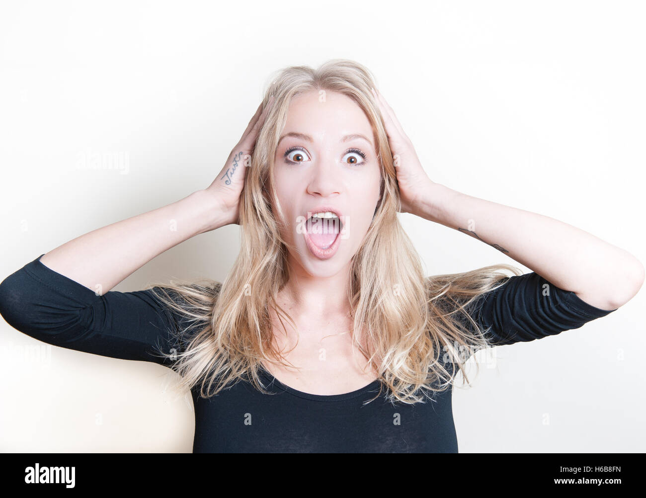 Young beautiful blond woman astonished stunned portrait, hands on head and open mouth Stock Photo