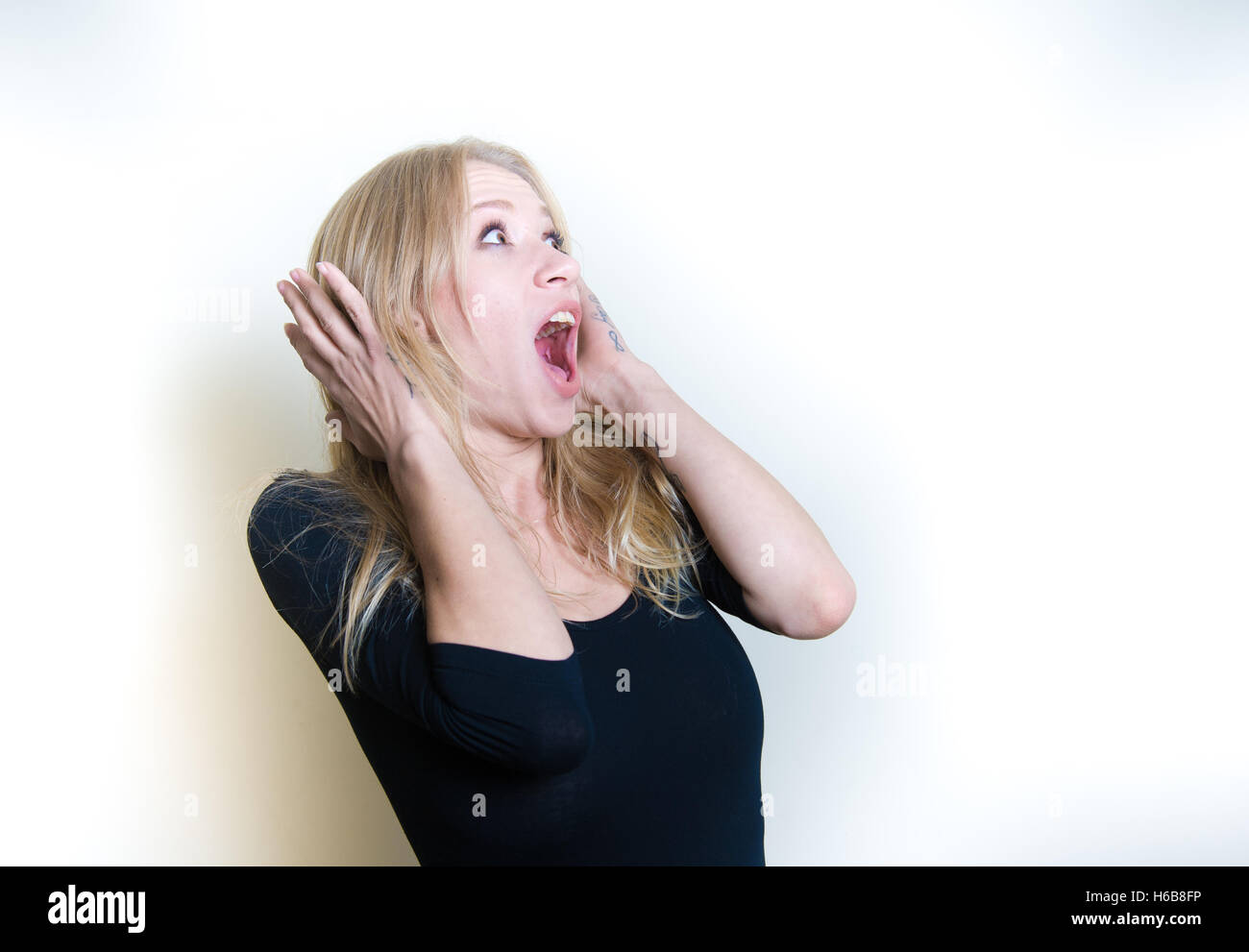 Young beautiful blonde woman astonished stunned portrait, hands on head and open mouth looking up Stock Photo