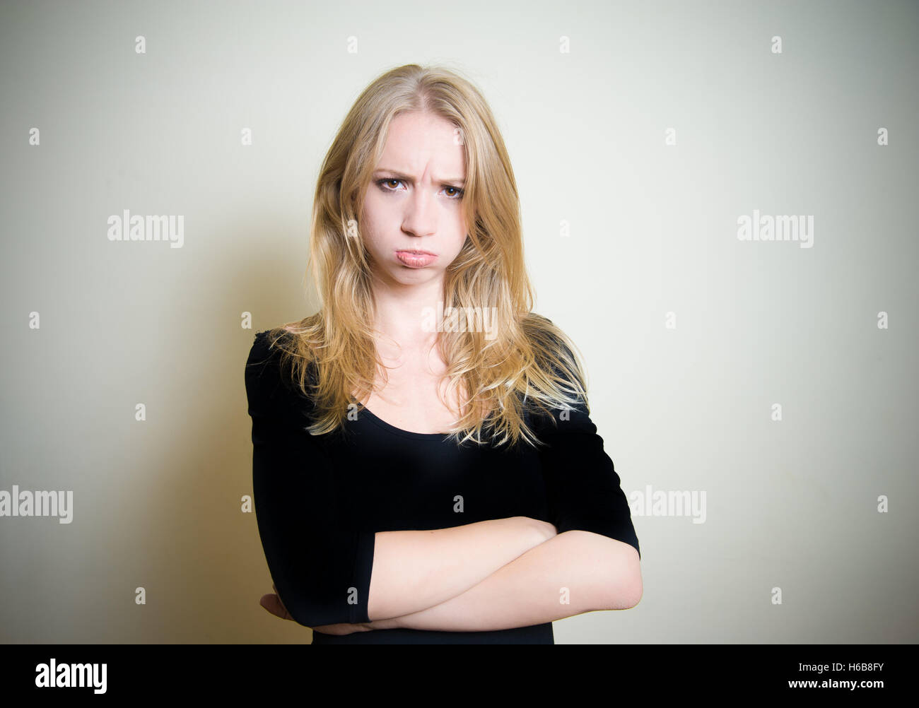 Young blonde attractive woman looking at camera, face expression angry, sullen, sulky, offended, peevish, clear wall in backgrou Stock Photo