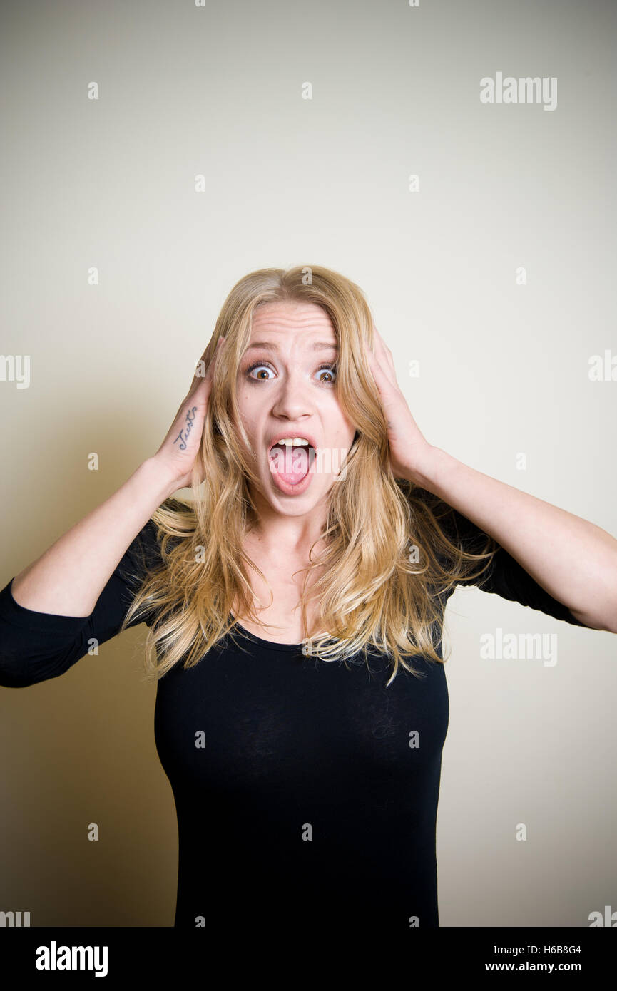 Young beautiful blonde woman astonished stunned portrait, hands on head and open mouth Stock Photo