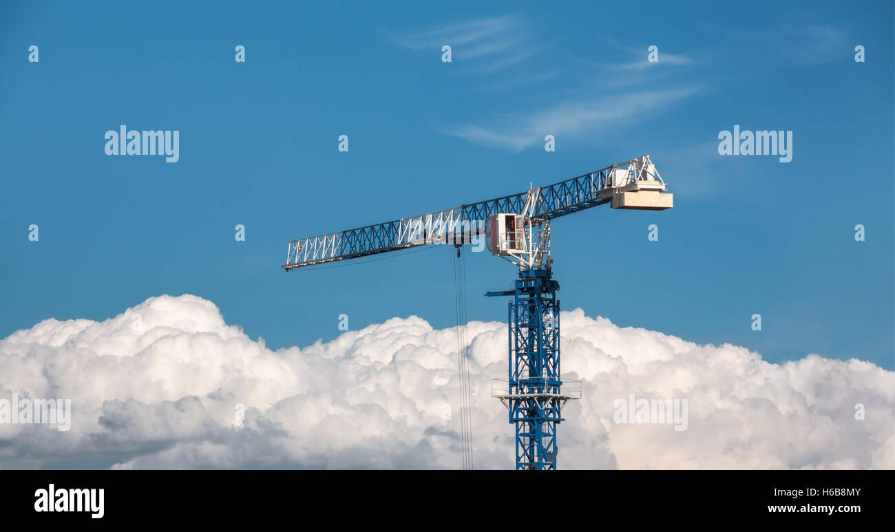Construction crane blue and white above the clouds on the blue sky