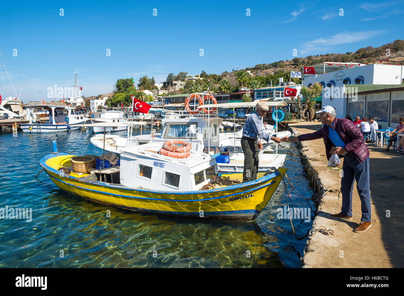 BODRUM, TURKEY - OCTOBER 10, 2016: Fisherman in traditional fishing boat takes payment from a customer in a fishing village. Stock Photo