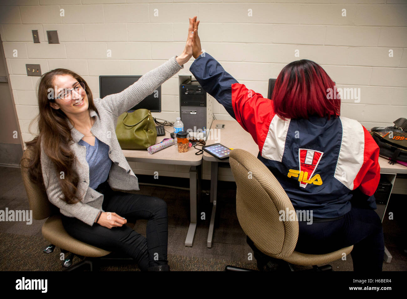 A Caucasian tutor in the learning center of a Santa Ana, CA, community college 'high fives' her happy Hispanic student in congratulation for her successful work. Note red dyed hair. Stock Photo