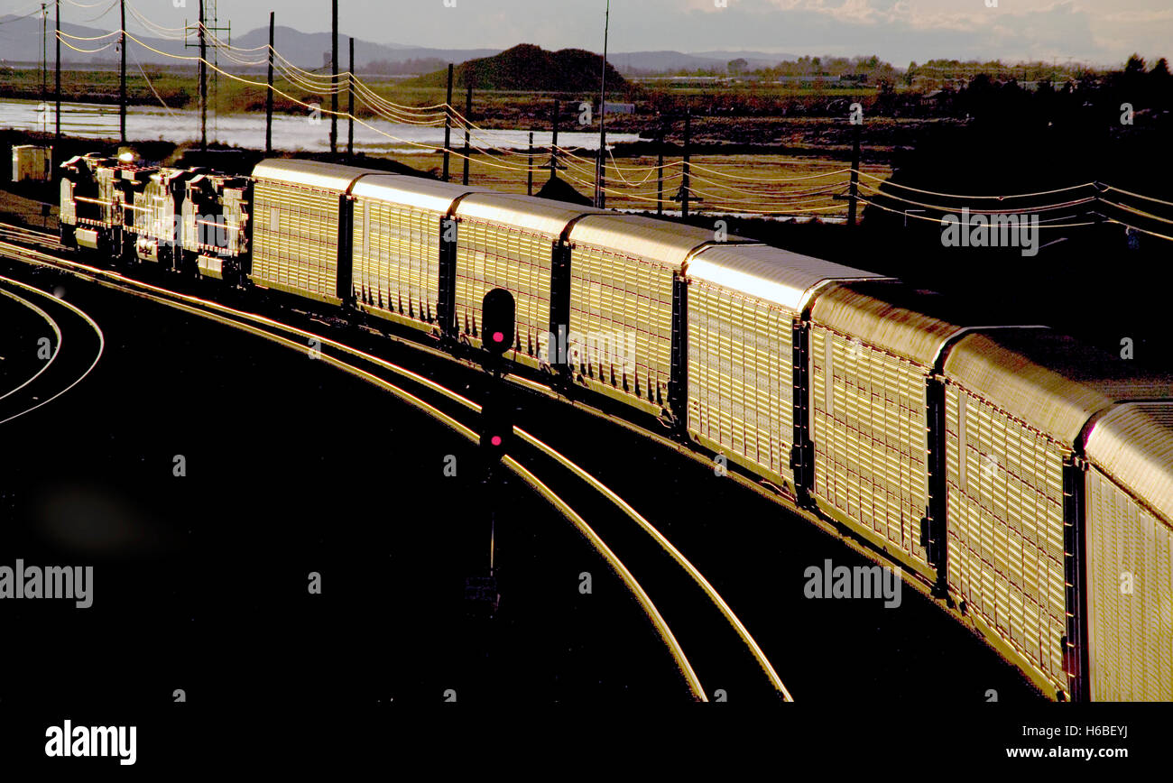 Afternoon sun shines on a freight train carrying livestock on a curve in Barstow, CA. Note red signal in center. Stock Photo