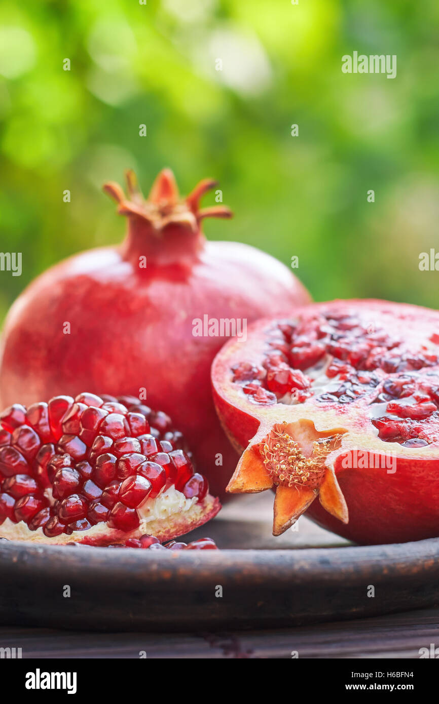 Ripe pomegranate fruit served on rustic plate in nature. Green blurry background with plenty of copy space Stock Photo