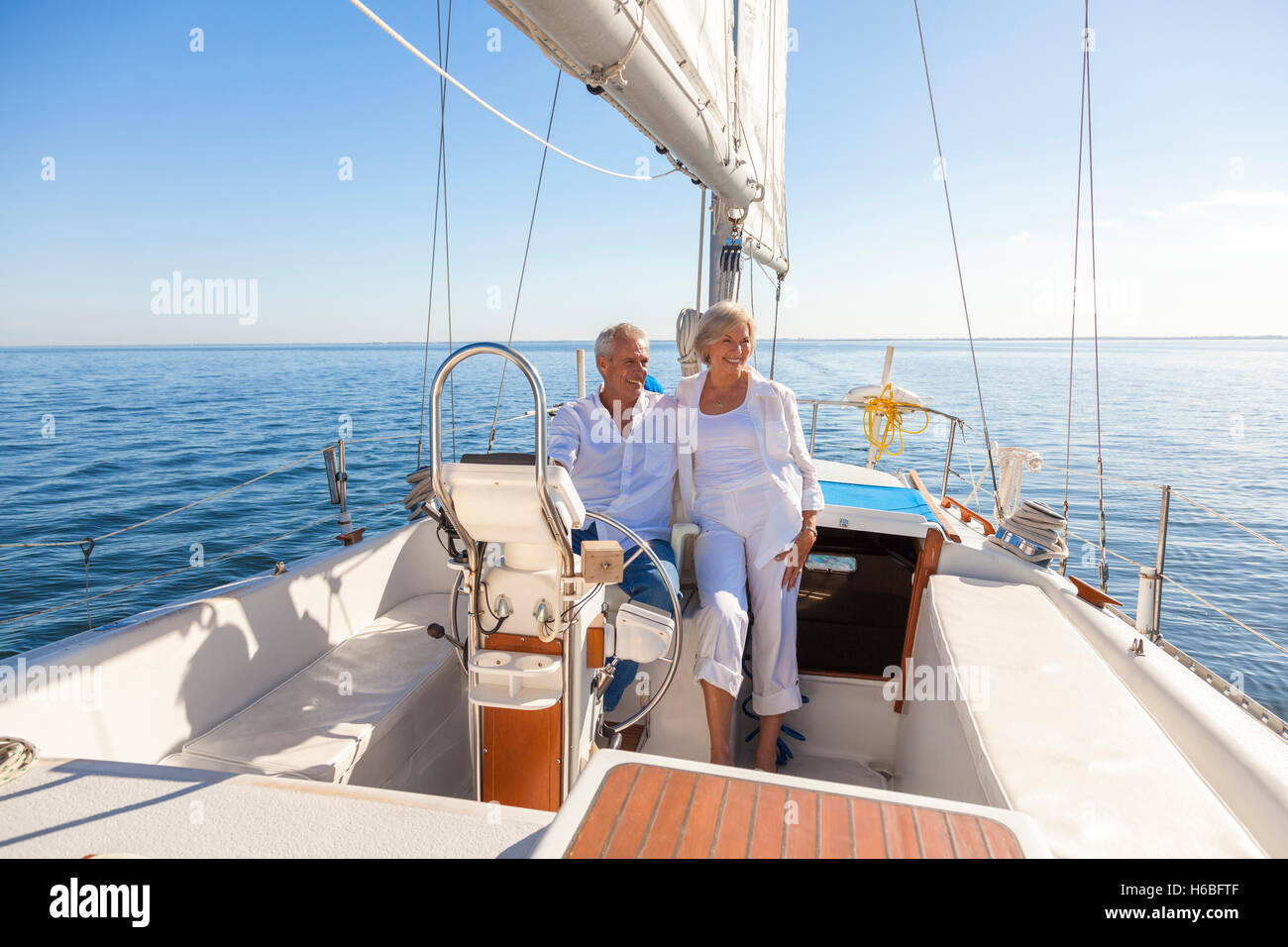 A happy senior couple laughing having fun sailing at the wheel of a yacht or sail boat on a calm blue sea Stock Photo