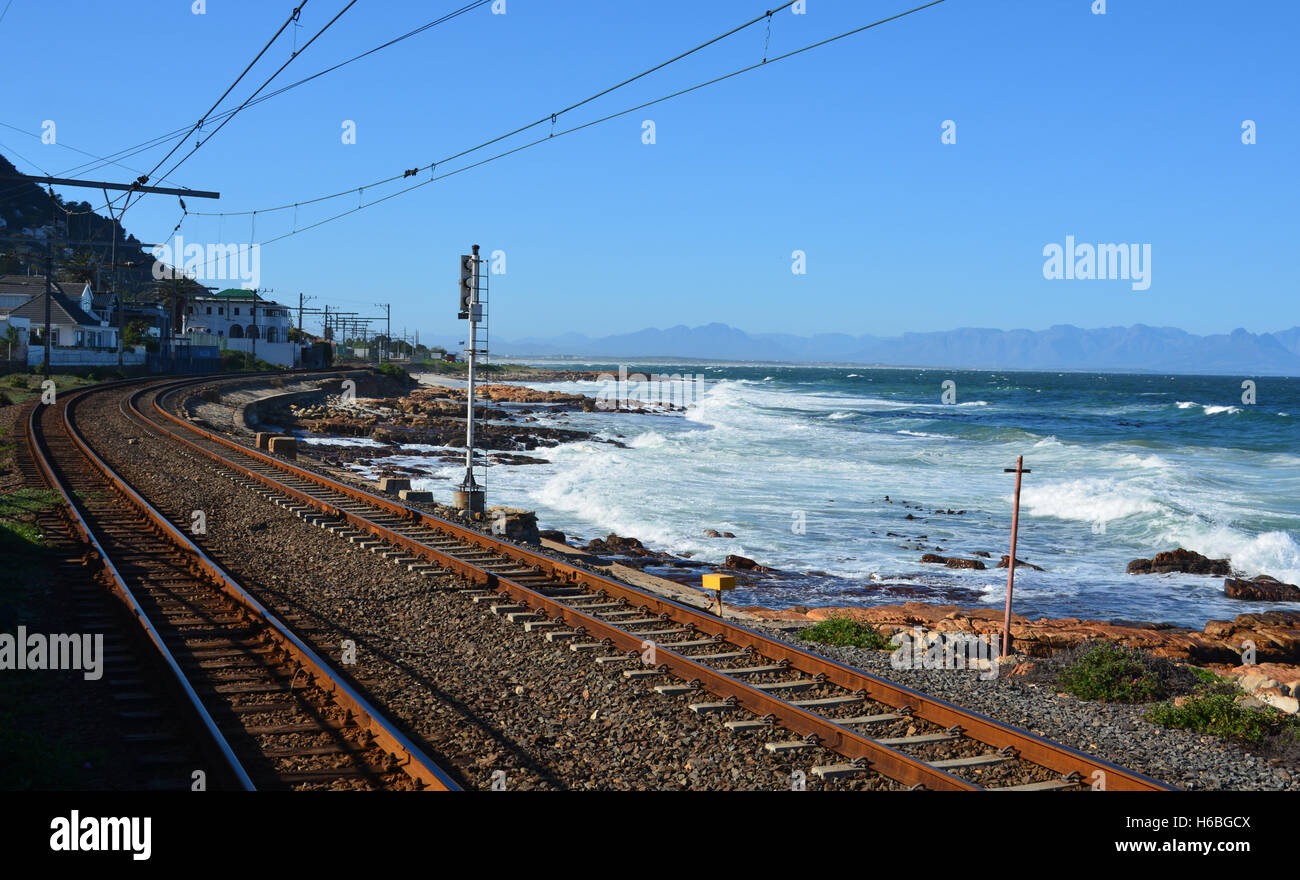 The Metrorail tracks hug the coastline of the False Bay heading north from the town of Kalk Bay into Cape Town South Africa. Stock Photo
