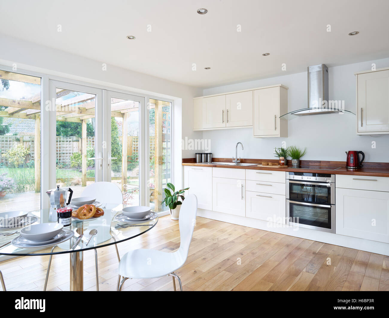 A contemporary, fresh open plan kitchen incorporating an integrated oven, cooker, hood & wood work surfaces. Oxfordshire, UK Stock Photo